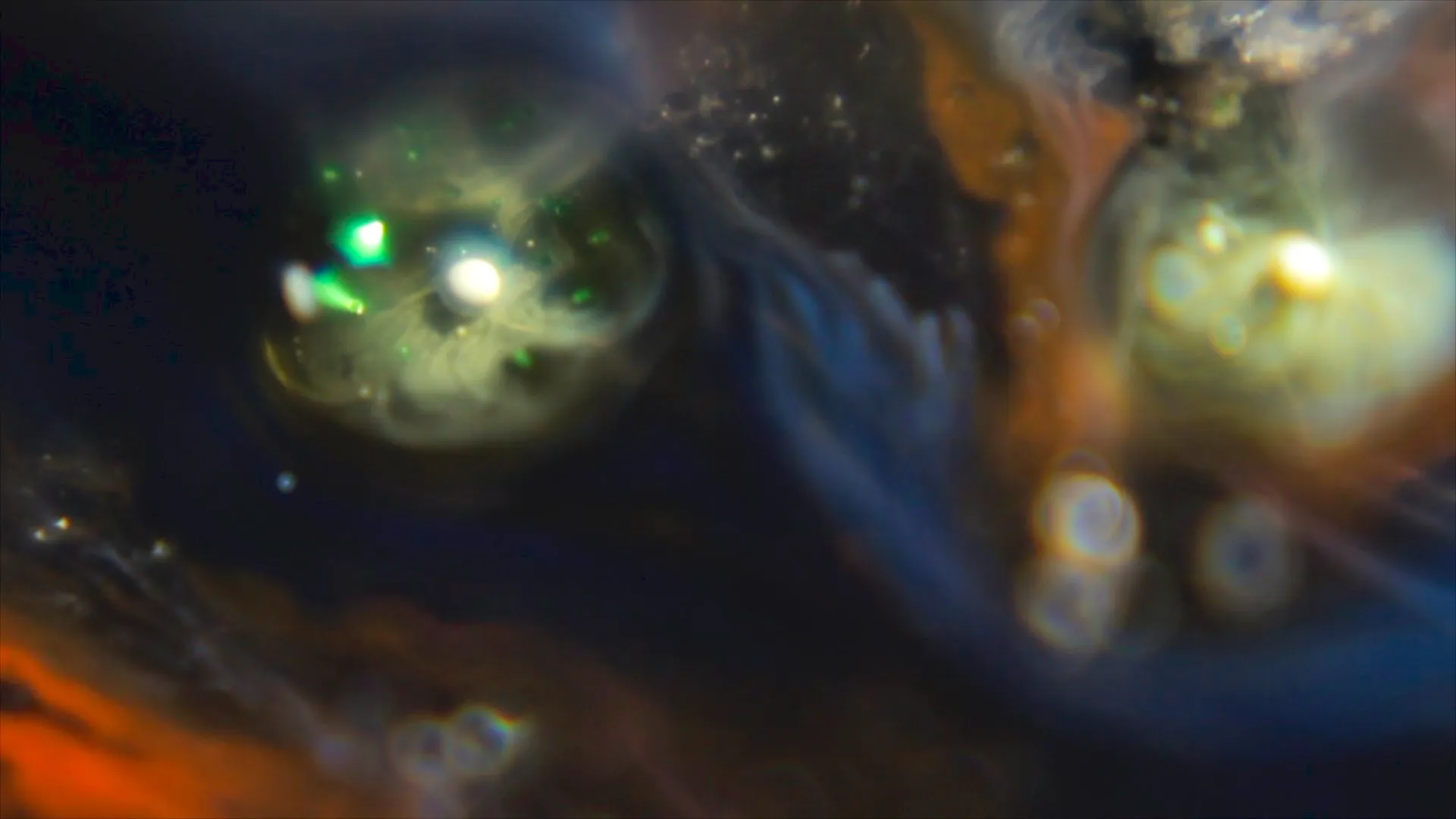 Fotograma de ALEPH ℵ0: formas luminosas verdes y ámbar suspendidas en un líquido azul oscuro.